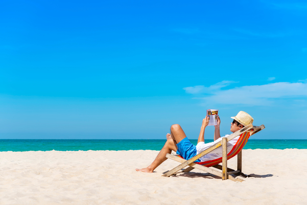 Person wearing straw hat lounging and reading a book in beach chair on the beach