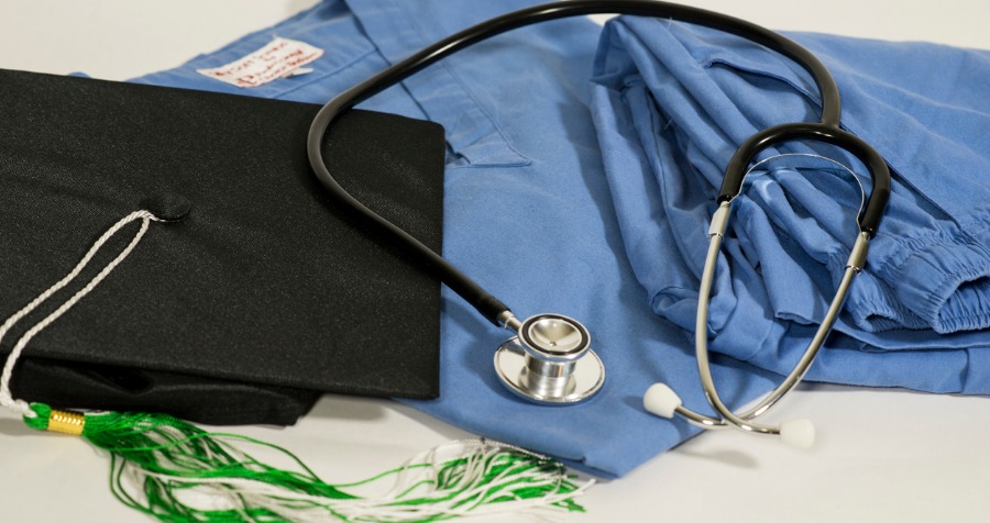 graduation cap next to scrubs and stethoscope