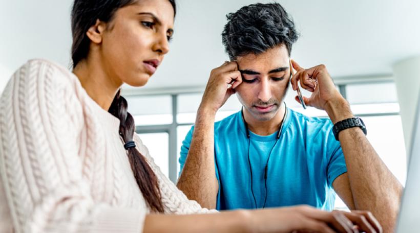 Two people sitting in front of computer, one is stressed out while the other types