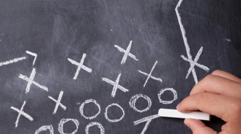 Hand writing football play in chalk on chalkboard