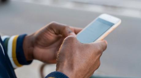 Person in casual jacket outside on sidewalk typing on smartphone